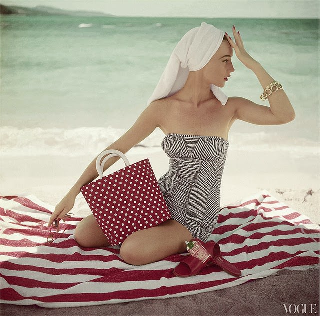 #58 Model seated on striped beach towel wearing grey and white patterned strapless bathing suit, 1954