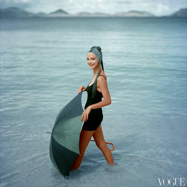 #64 Gretchen Harris, standing in ocean with open green and blue umbrella, wearing knitted black maiilot of DuPont and water-velvet cap , 1957