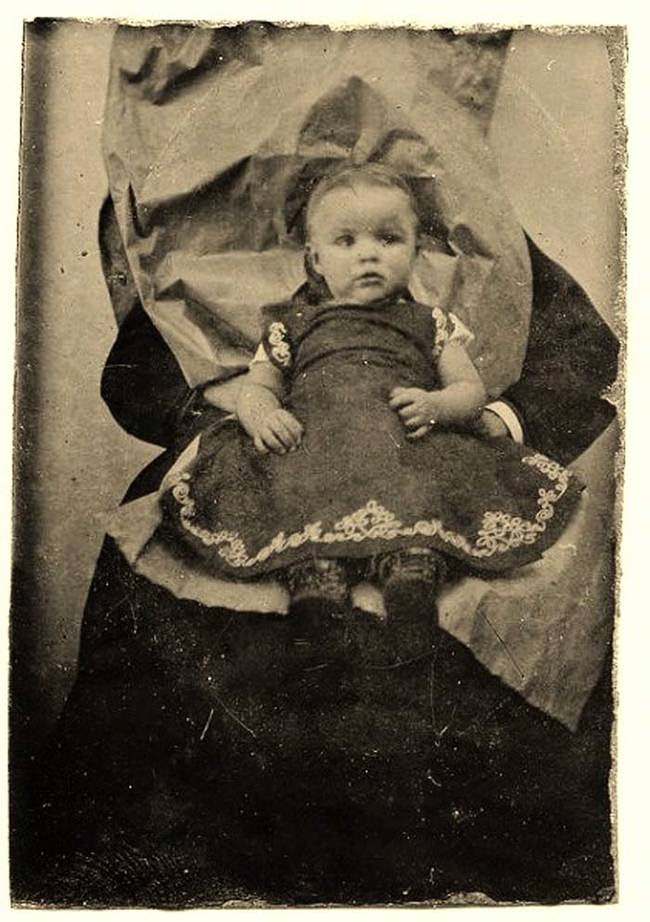 A little girl sitting on someone’s lap. The person held her in place while the photo was taken.