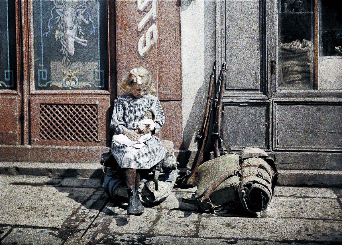 A girl holds a doll next to soldiers’ equipment in Reims, France, 1917