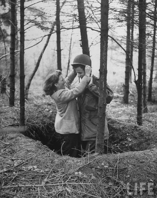 #18 Ernie Kreiling gets helmet put on his head by his laughing wife in the foxhole where he first heard an enemy shell during their vacation tour of battlefields were he fought during WWII in North country.