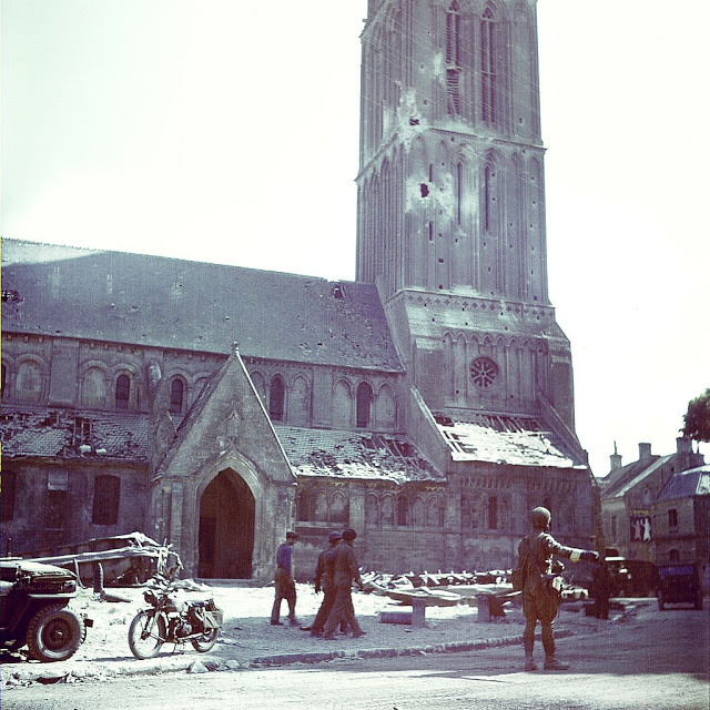 #50 A Canadian soldier directs traffic in front of the Notre-Dame Nativity church, in Bernieres-sur-Mer.