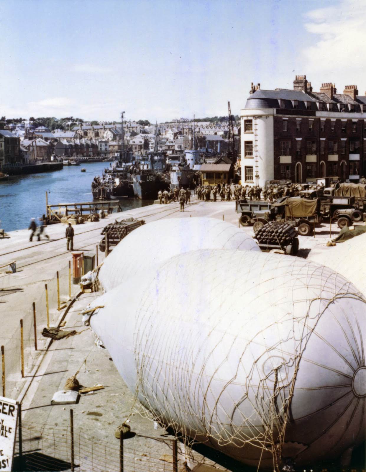 #55 American troops load onto LSIs at a port in Britain where barrage balloons have been anchored for protection against strafing and low level bombings.