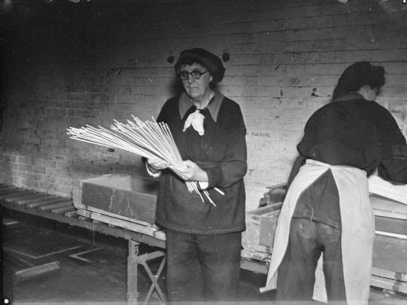 #19 An elderly female munitions worker at the Royal Naval Cordite Factory at Holton Heath counts sticks of cordite before they are packed by her colleague into boxes ready for distribution to various naval armament depots.