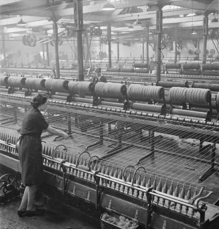 #13 A textile worker stands at the spinning mule. The wooden rollers are transferred from the condenser to the spinning mule which is the means of twisting and stretching.
