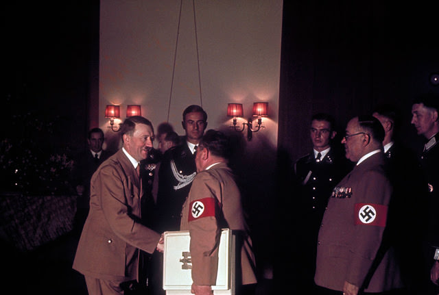 #63 Adolf Hitler shakes hands with one of his personal photographers, Heinrich Hoffmann, while his doctor, Theodor Morrell (right) waits to greet the Fuhrer on Hitler’s 50th birthday, April 20, 1939
