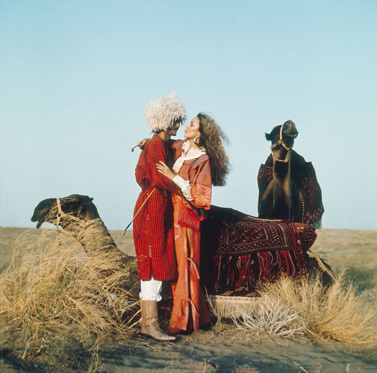 #26 Jerry Hall embracing a man surrounded by two camels, 1975