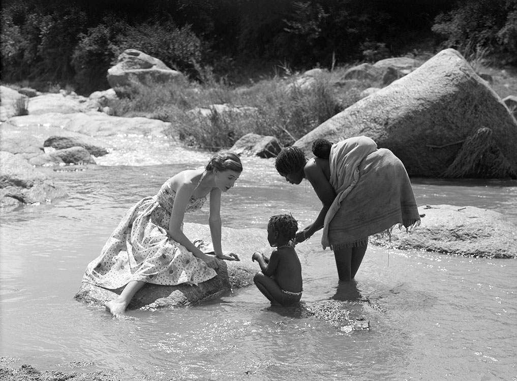 #51 Wenda Parkinson wearing a dress by Susan Small and is photographed with a mother and her children for Vogue, 1951