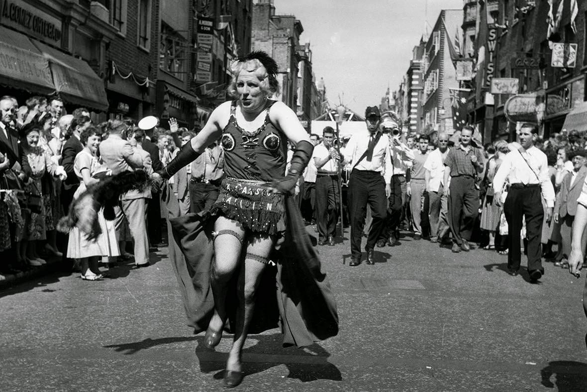 #17 A man in drag heads a carnival procession down Old Compton Street during the Soho Fair, 1956