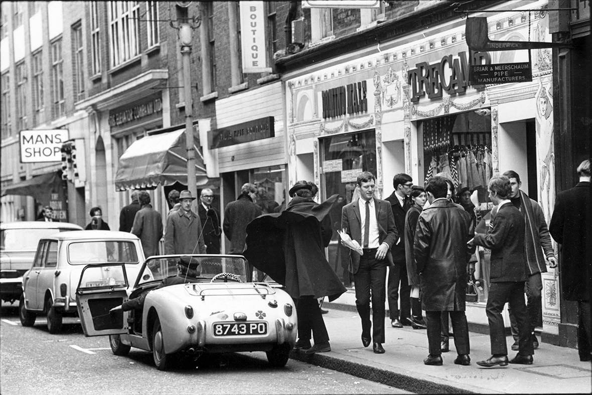#26 A man sweeps his cloak around him after getting out of a sports car on Carnaby Street, 1966