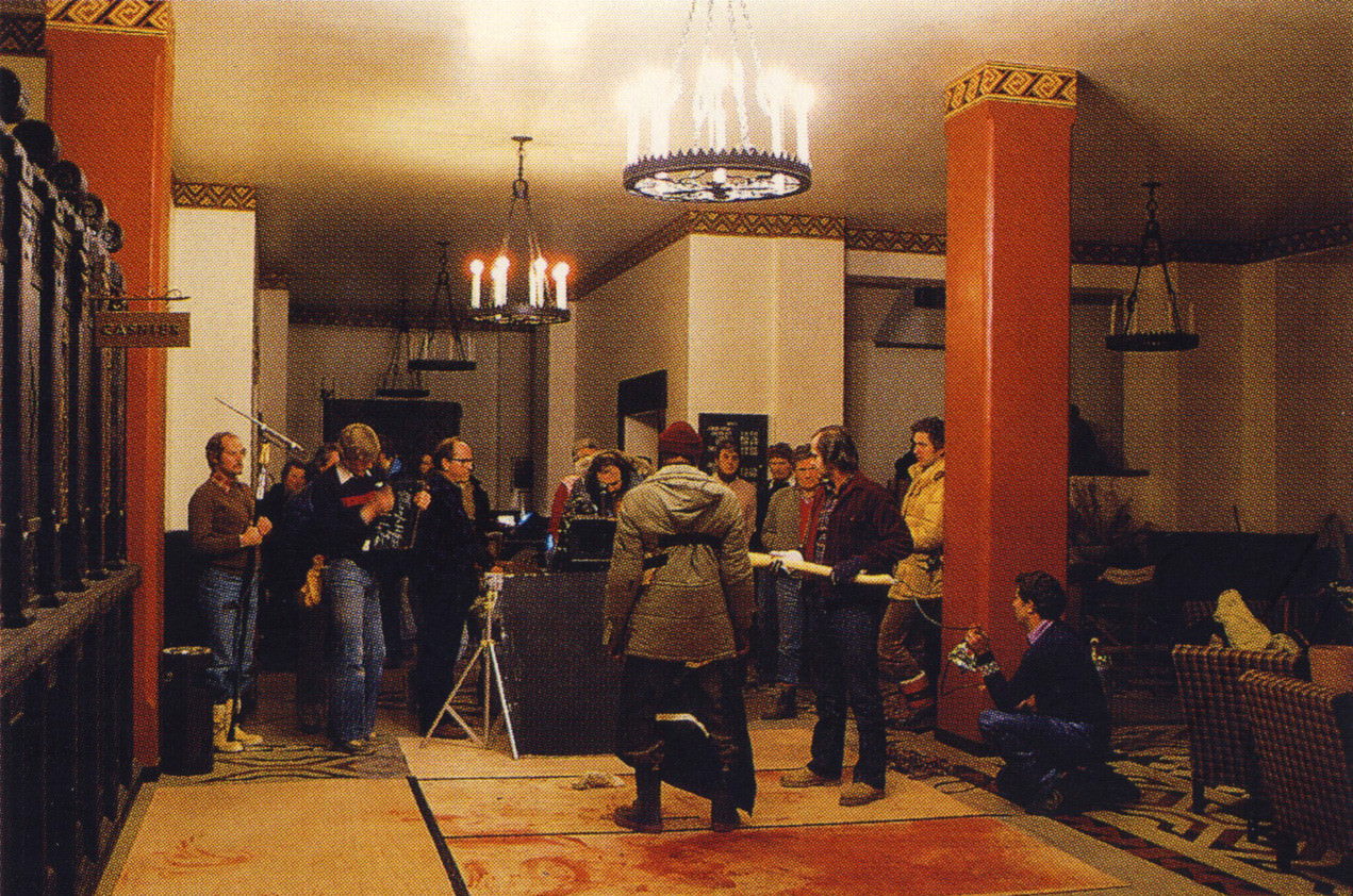 #33 Filming Dick Hallorann’s death scene on the lobby set. Stanley Kubrick composes the insert shot of the axe striking Hallorann’s chest. A special effects artist kneeling to the right of Jack Nicholson holds a bag of fake stage blood, with tubing to deliver the blood running up the handle of the axe.