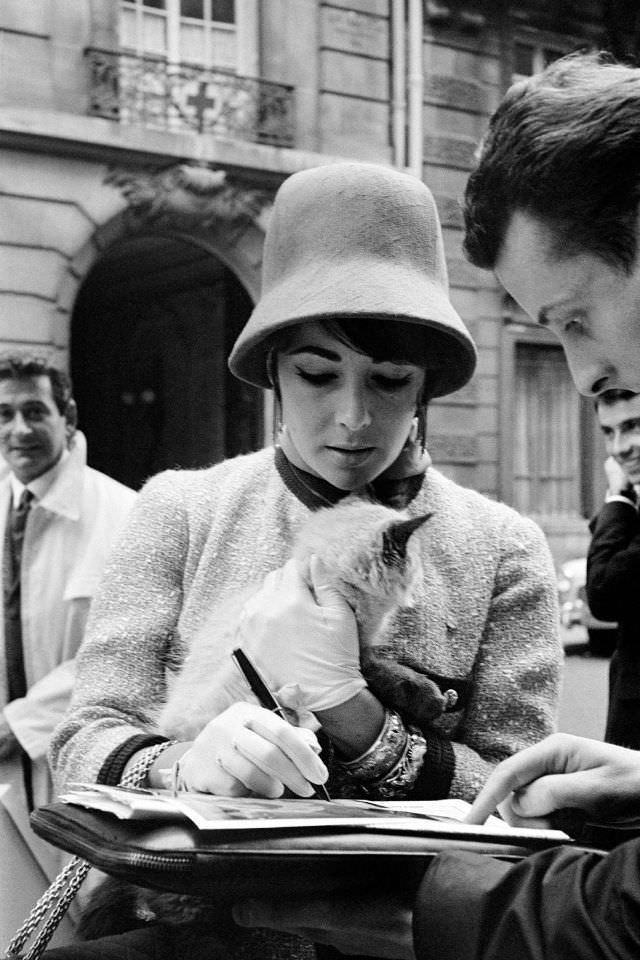 #22 While returning to Paris from a trip to Russia, Taylor proved herself capable of simultaneously signing an autograph and stroking the nape of a mysterious cat, 1961