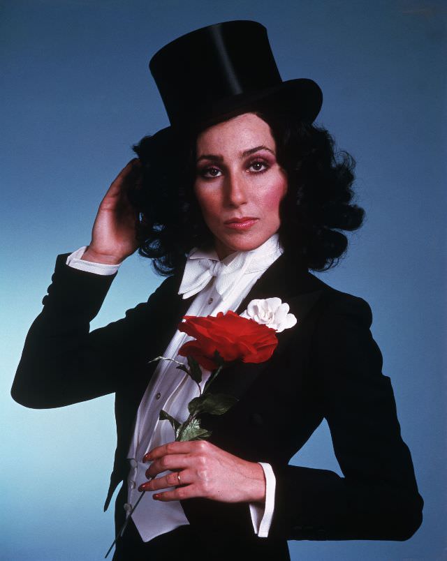 #22 Cher, wearing a tuxedo and top hat, holds a red rose. Photo by Bettmann, 1975