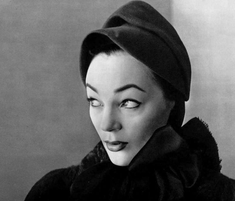 #4 Ivy Nicholson in red felt cap tied with large red satin ribbon by Caroline Reboux, fur coat by Maurice, 1951