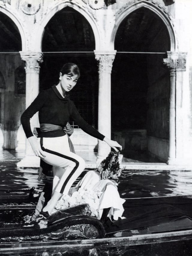 #43 Ivy Nicholson in narrow pants and sweater shown here standing in a gondola in front of Ca’ d’Oro, Venice, 1956