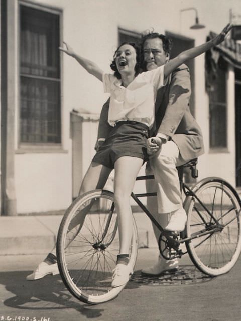 #24 Andrea Leeds and Edward Arnold riding a bike, 1936