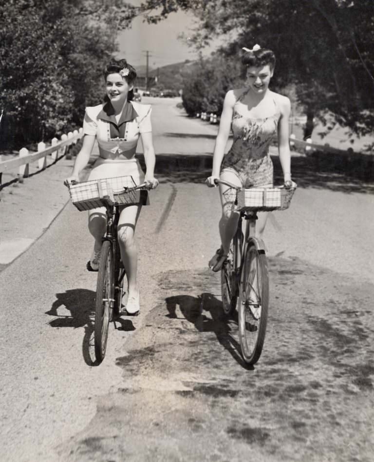 #7 Marguerite Chapman and Leslie Brooks ride bikes.