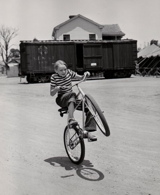 #42 Claude Jarman Jr. wheelies a bike.
