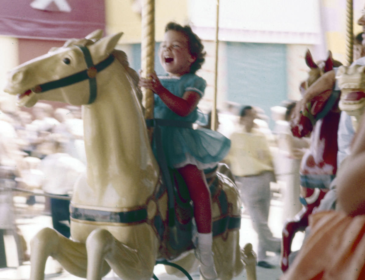 #24 A little girl laughs with excitement while riding a carousel at Disneyland in July 1955