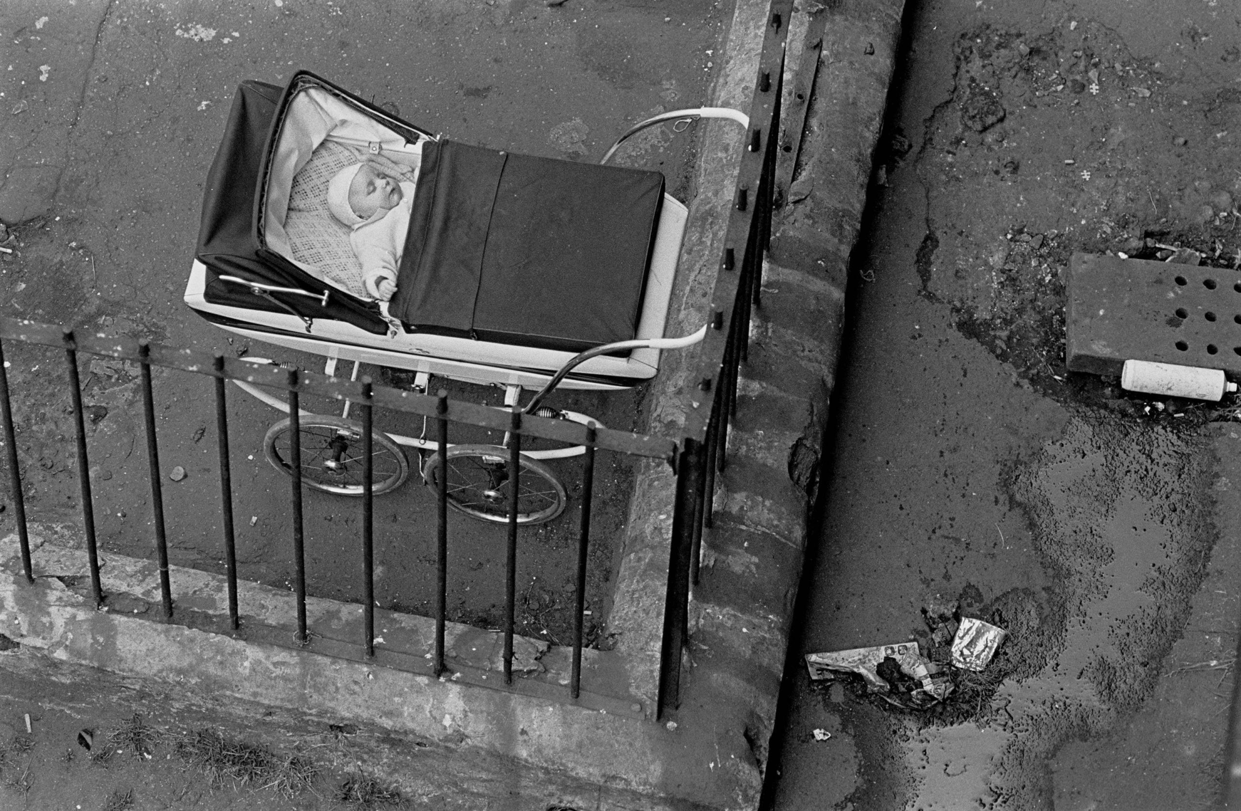 #16 Baby sleeping by the drains in a tenement courtyard Glasgow Maryhill 1971