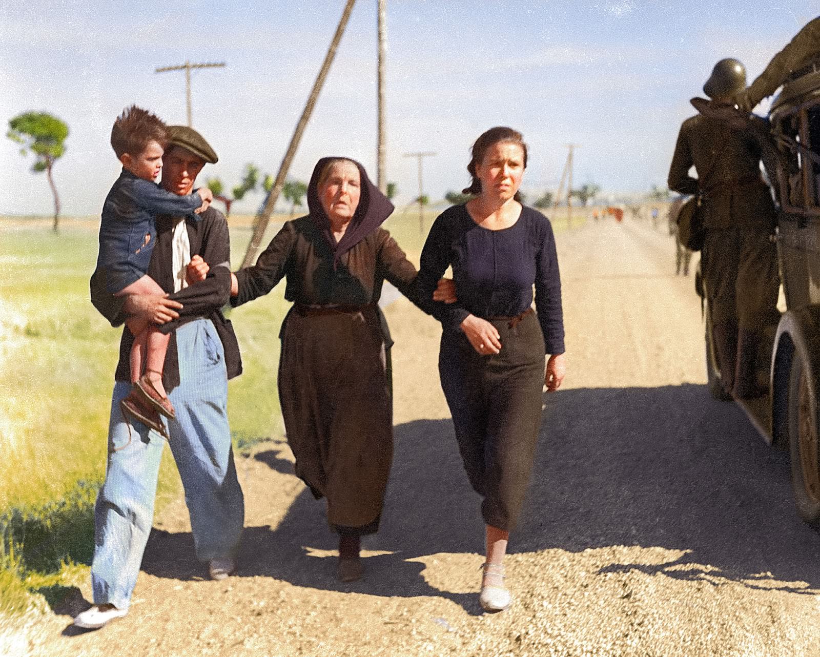 #11 A family of Belgian refugees hold and support each other as they pass a military vehicle while walking the road to France, circa 1940. Behind them are other groups of refugees fleeing occupied Belgium.