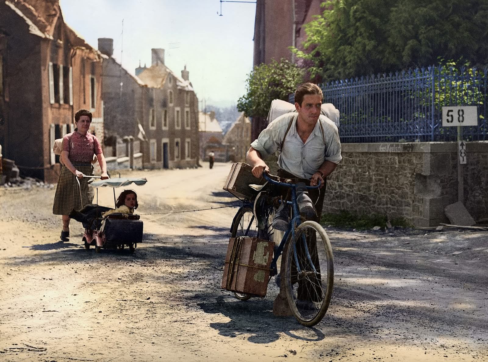 #13 A man pulls a refugee’s pram, attached by a cord to his bike, up a hill in Roncey, France on August 7, 1944.