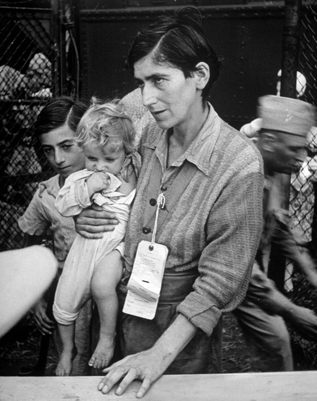 #1 Swiss Jew Eva Bass, formerly a nightclub singer in Paris, entering refugee camp at Fort Ontario, with her children Yolanda and Joachim, whom she carried on a 60-km trek through the fighting lines to reach the American transport ship Henry Gibbins. 1944.