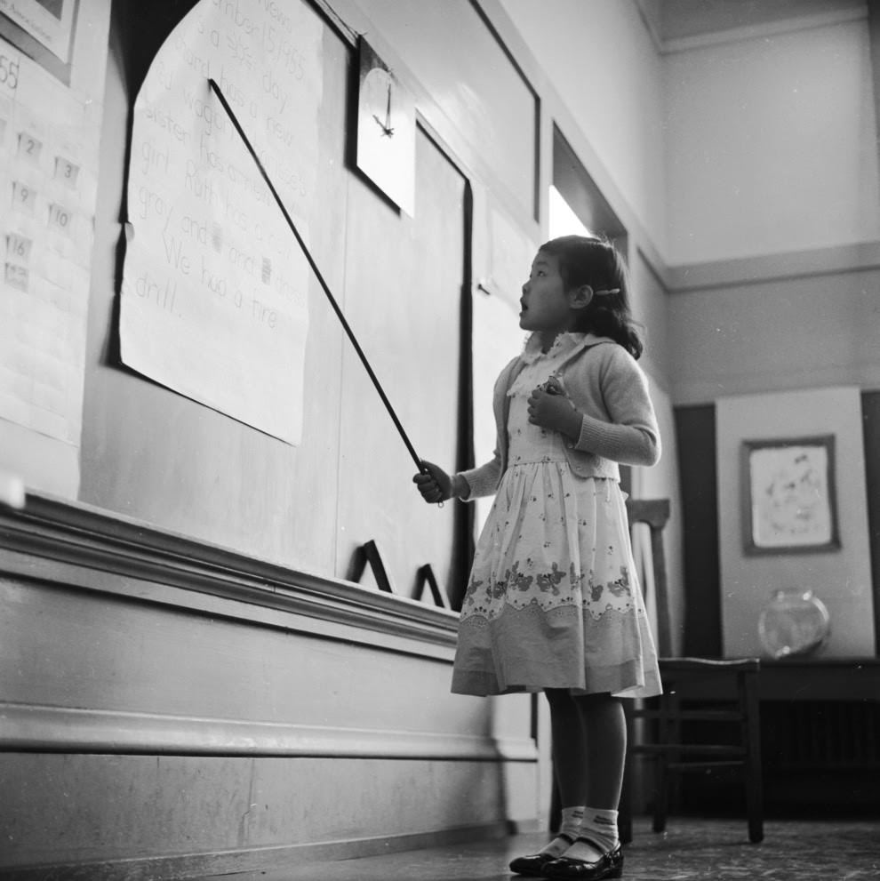 #37 A little girl reads aloud from the blackboard.