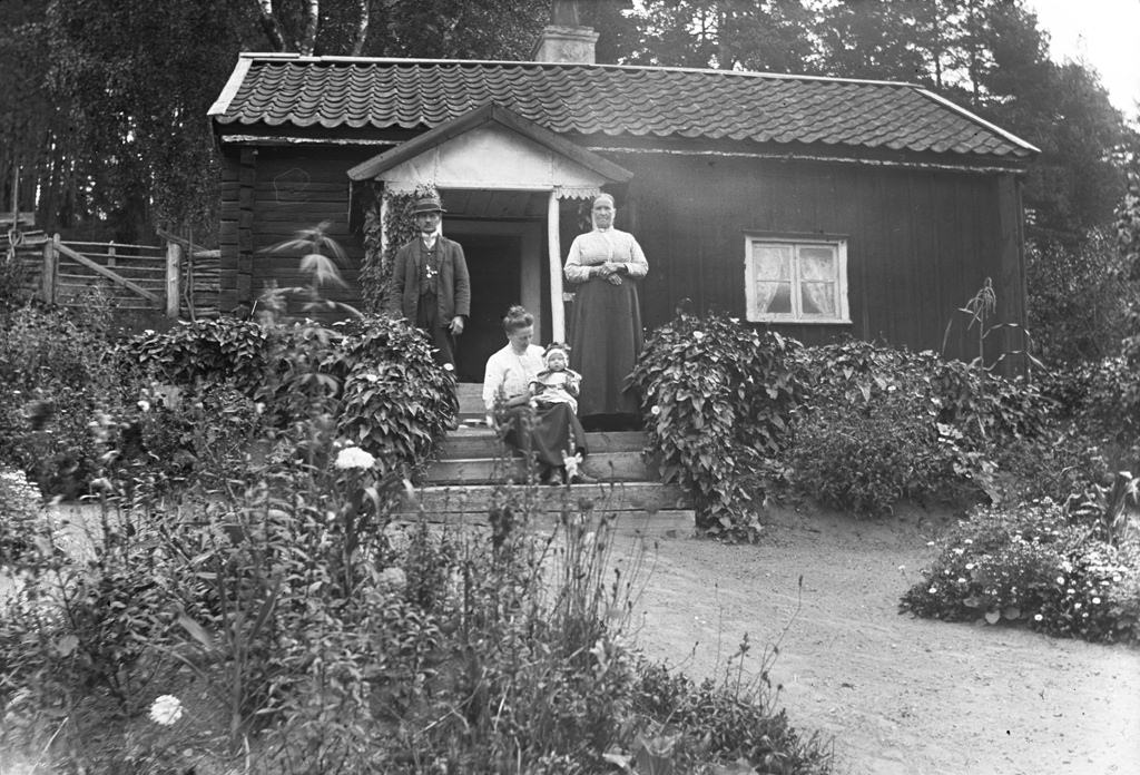 #39 Rakelt, Vrångsjö 1913. Rakelt or Peraklet was a cottage in Vrångsjö manor in Marbäck. The picture shows torparparet Gustav Engdahl (b. 1850) and Augusta Engdahl (b. 1848) and their daughter Esther Engdahl (b. 1888) and her daughter Marta Linnea Ingegerd (b. 1913).