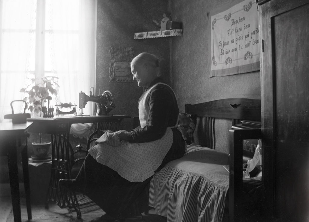 #58 The woman at the sewing machine is Emelie Castensson (born 1854), who married with a slipper-maker Johan Andersson. The couple lived here when the picture was taken in Vagnsvik, Frinnaryd.