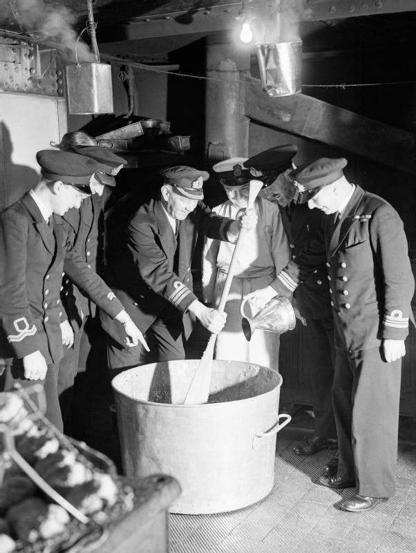 #40 The captain of a destroyer depot ship in the Home Fleet at Scapa Flow stirring the Christmas pudding, while the First Lieutenant adds a tot of rum, 12 December 1942.