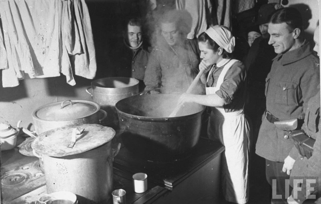 #60 Finnish soldiers watching a woman stirring the pot for Christmas dinner, Finland, 1939.