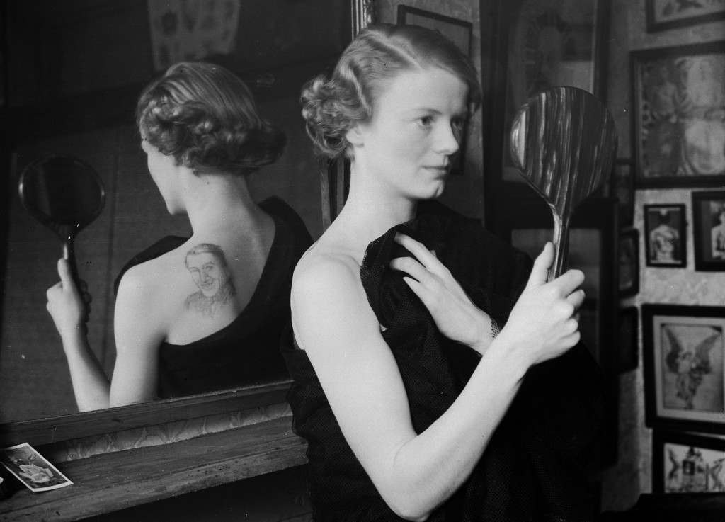 #14 A film fan uses a mirror to admire the image of film star Gary Gooper she has had tattooed on her back by George Burchett a London tattooist, 1936.