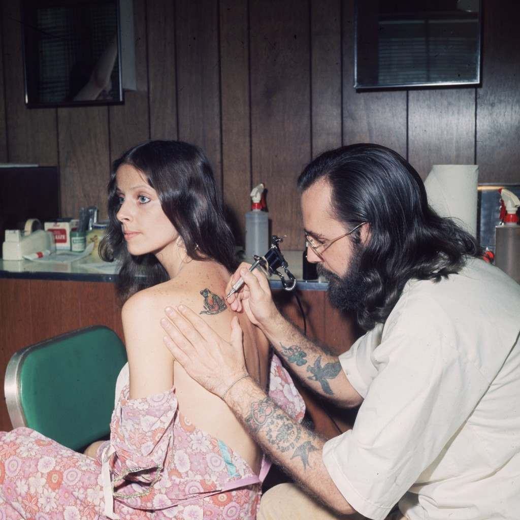 #19 An American tattoo artist working on a client’s shoulder, 1973.
