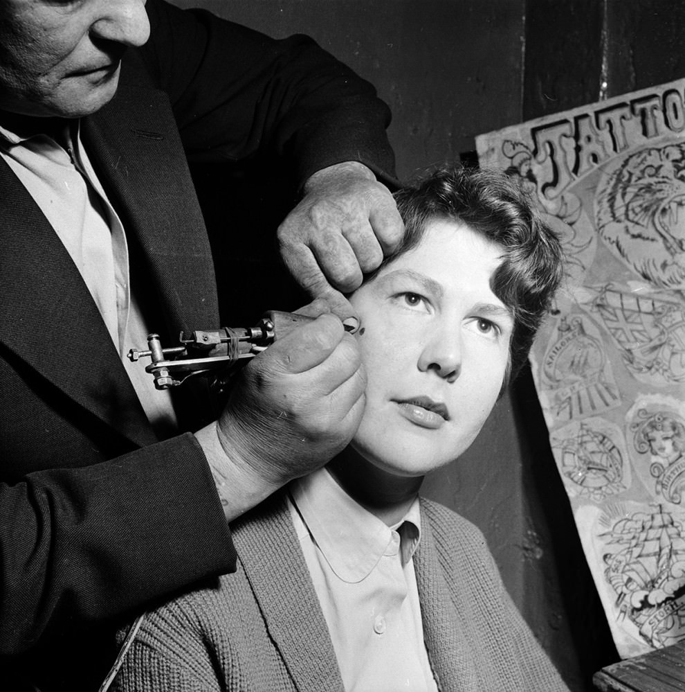 #9 A tattoo artist paints a permanent beauty spot on the cheek of a woman at his workshop in Copenhagen in 1956.