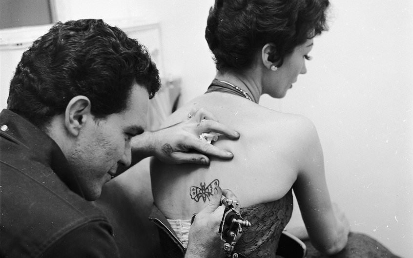 #28 A tattoo artist tattooing a butterfly onto Lulubelle Hostein’s back, ca. 1955