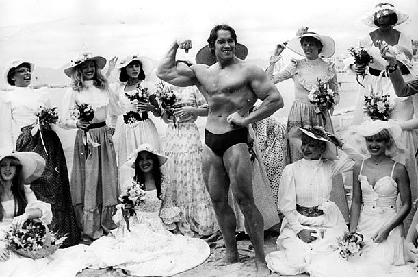#68 Arnold Schwarzenegger, the film actor who first became famous as Mr Universe for his magnificent physique, on Cannes beach during the Film Festival with the girls from the Folies Bergere.