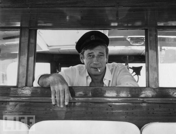 #25 Yves Montand regards his passengers on board his yacht at Cannes during a holiday on the Cote d’Azur on July 28, 1965.