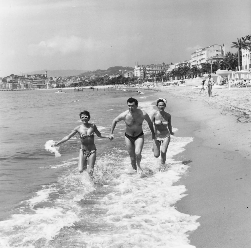 #46 George Baker runs through the surf at Cannes with Bella Darvi and another young friend, 1956.