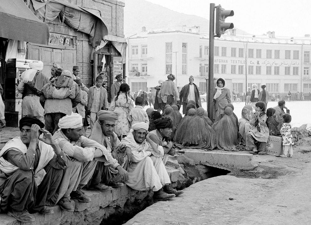 #12 A modern traffic light stands incongruously amid burqa-clad women sitting on a Kabul street corner with their backs to their men on May 25, 1964.