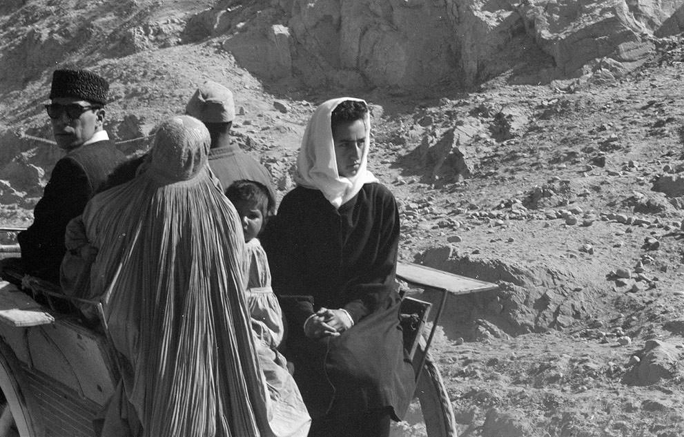 #13 Afghan women, men, and child in traditional dress ride in a cart through an arid, rocky landscape, November, 1959.