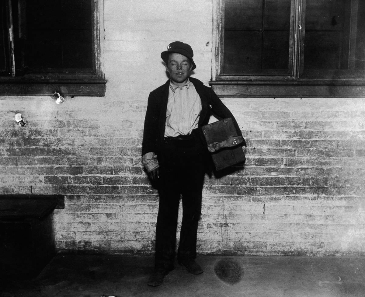 #18 A shoeshine boy named Tommy holds his shoeshine kit on a sidewalk, 1890