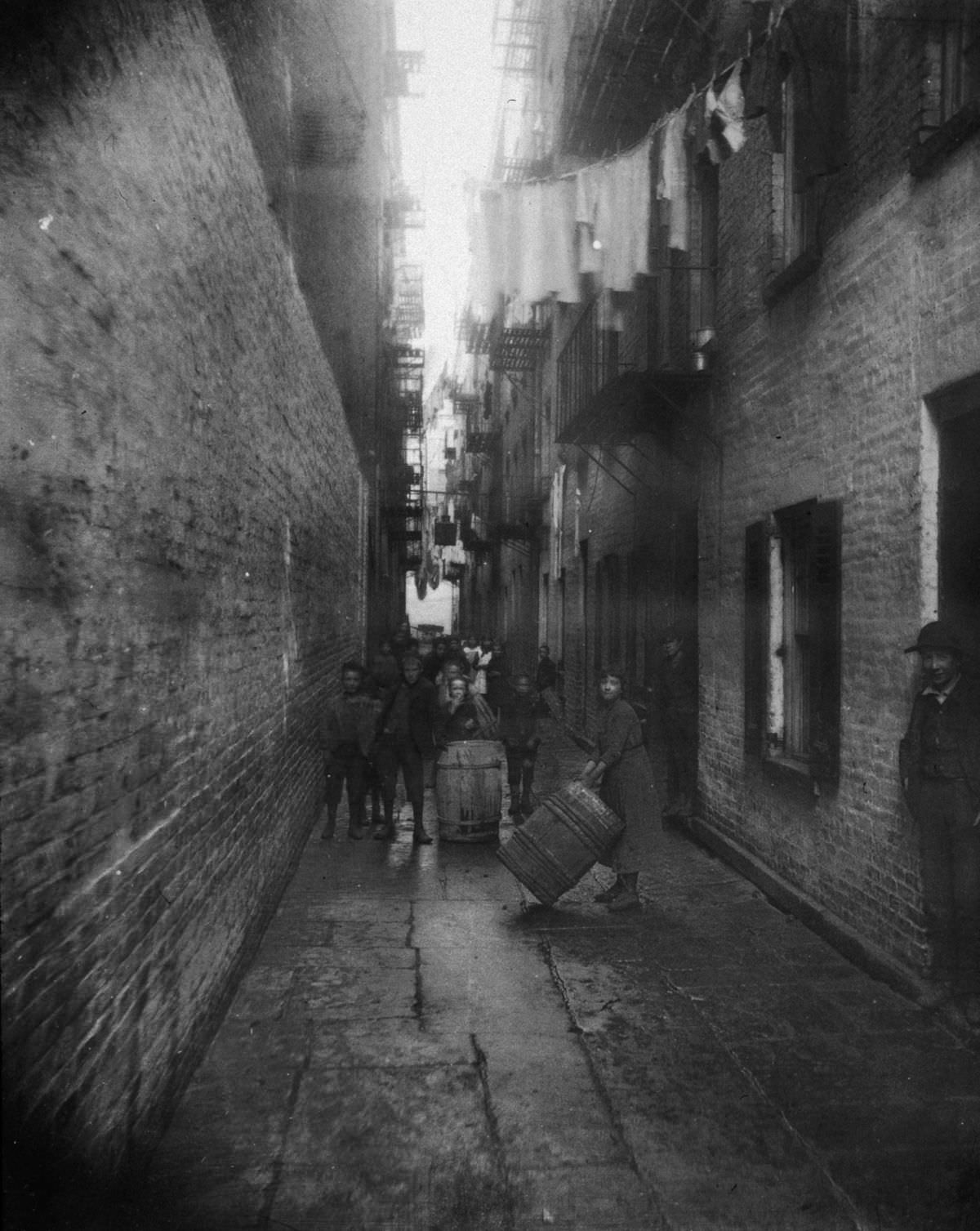#23 Children play with barrels in an alley between tenement buildings in Gotham Court, 38 Cherry Street, 1890
