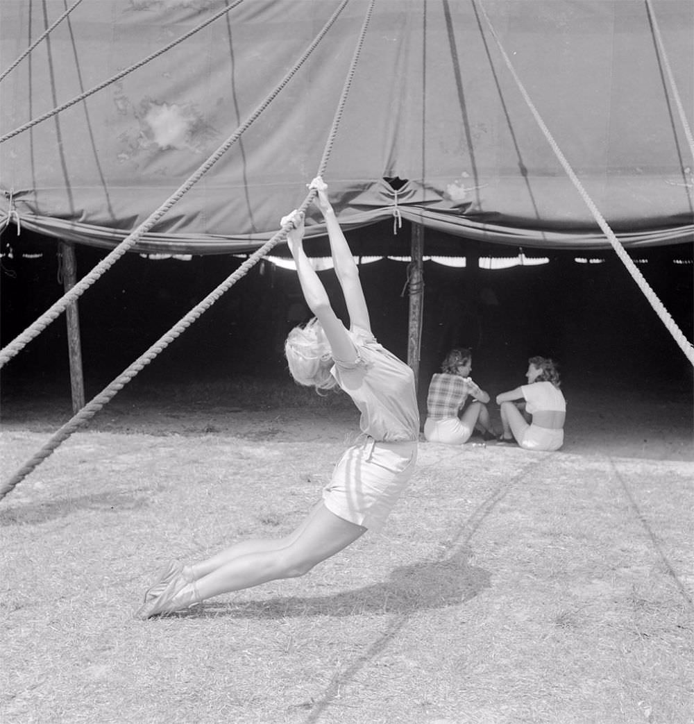 An acrobat practicing with a tent rope while two girls are sitting nearby during a rehearsal for the Ringling Bros. and Barnum &; Bailey Circus in Sarasota, FL in 1949.