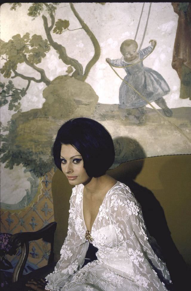 #4 Sophia Loren wearing a white dress, sitting in front of a painting in her villa.