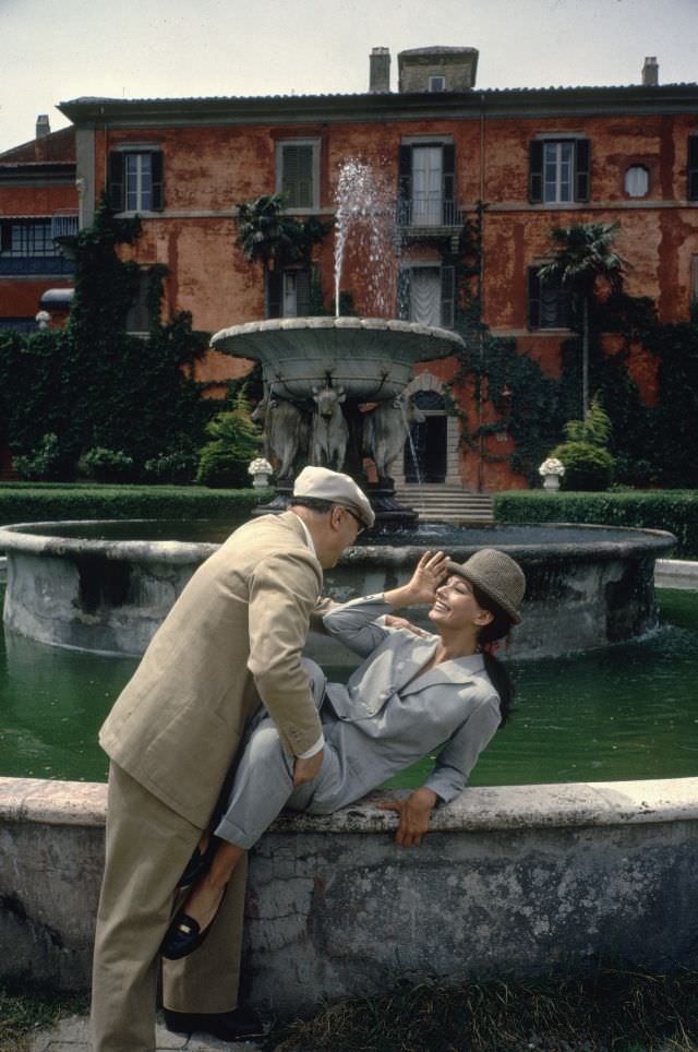 #16 Sophia Loren and Carlo Ponti posing in front of a large fountain at their villa.