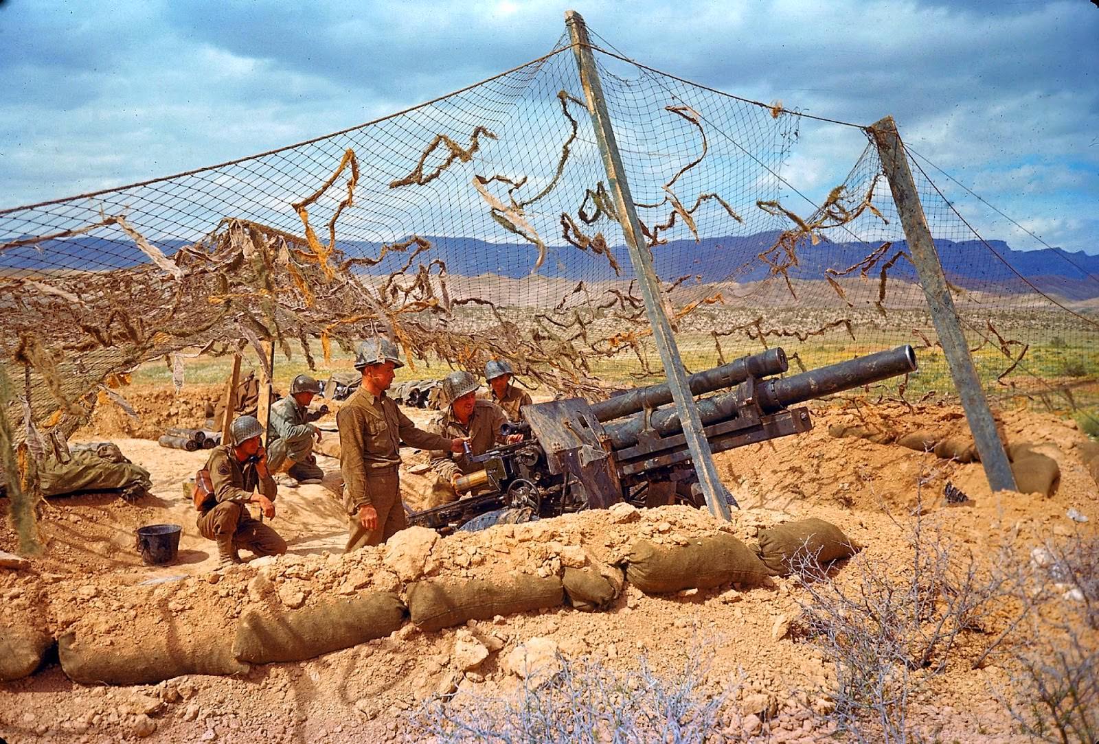 #38 An American gun crew in camouflaged emplacement awaiting orders to fire during the desert fighting between German and American forces in the El Guettar Valley in 1943.