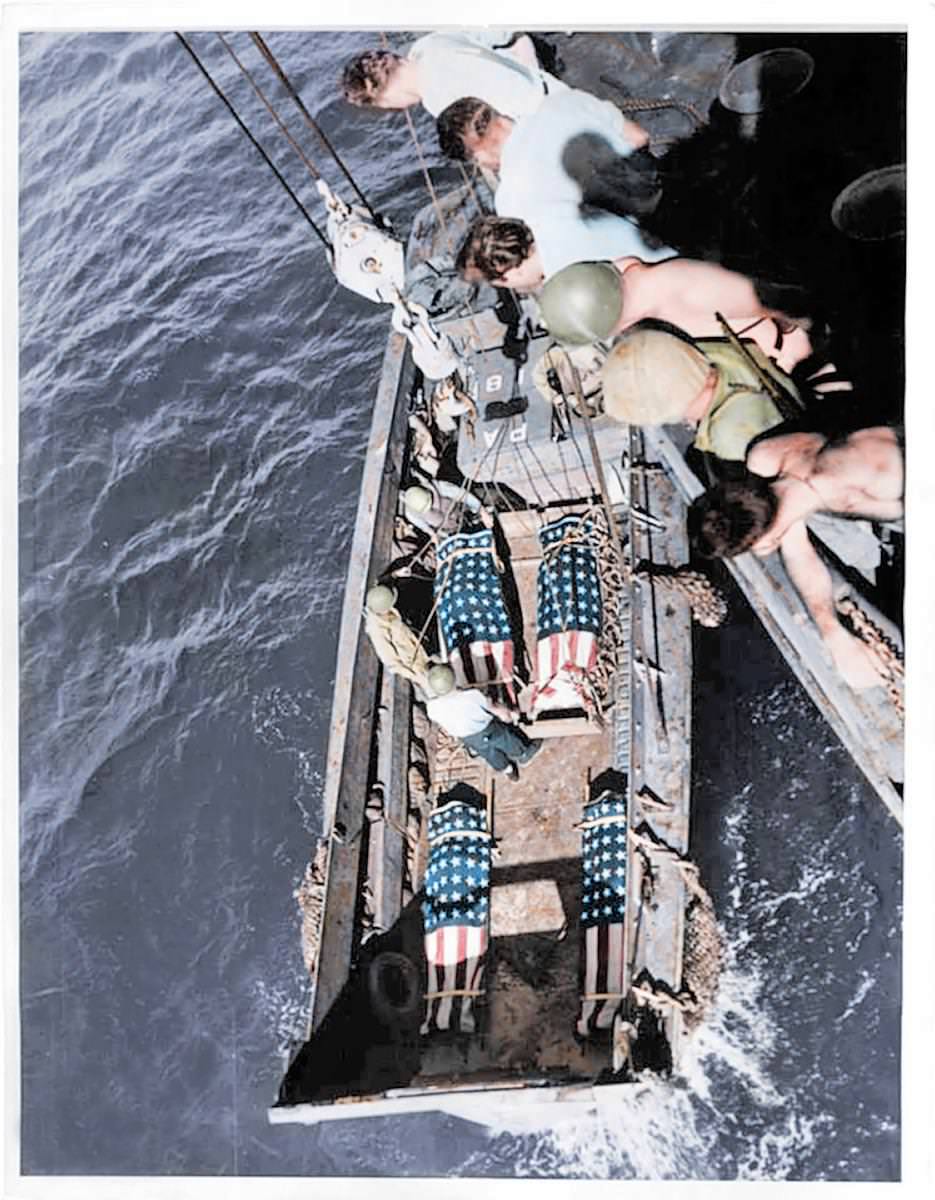 #48 Deceased US soldiers are wrapped in their national flag and carefully lowered down onto a ship by comrades ready for burial.