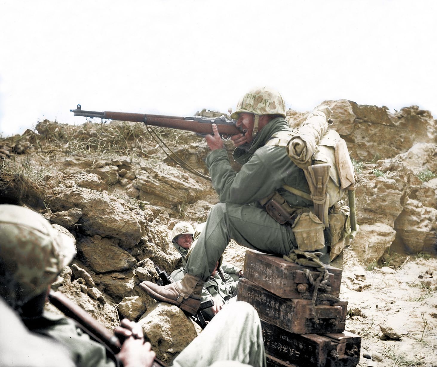 #61 A US marine takes aim while sitting on Japanese ammunition boxes.