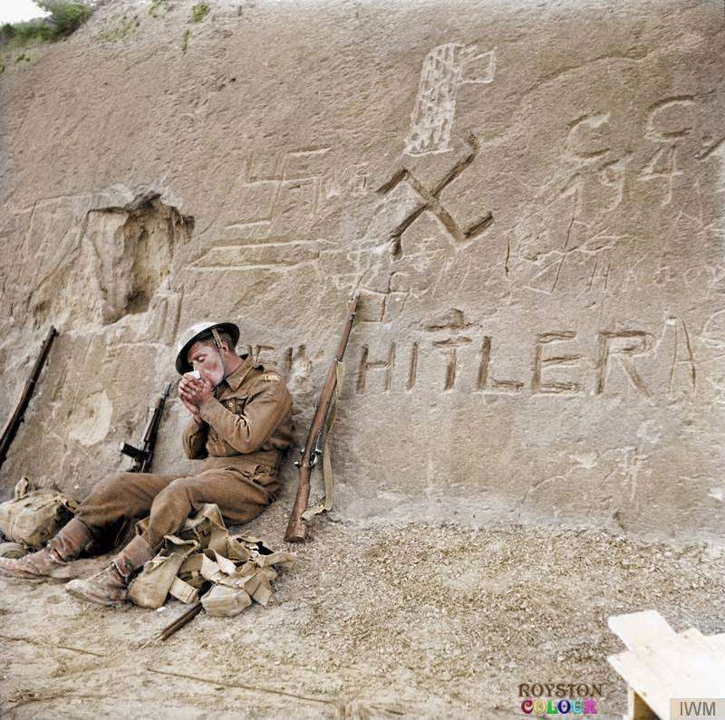 #78 Allied Soldier takes a break during the approach to Tripoli, Libya beside a swastika and the words ‘Heil Hitler’ that have been carved into a rocky hillside during January 1943